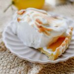 A homemade Lemon Meringue Tart with a buttery pastry crust filled with silky fresh lemon curd and topped with toasted Italian meringue, served on a white cake stand with fresh lemons and soft summer décor.