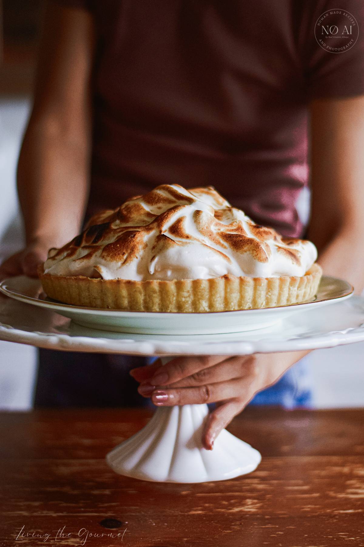 A homemade Lemon Meringue Tart with a buttery pastry crust filled with silky fresh lemon curd and topped with toasted Italian meringue, served on a white cake stand with fresh lemons and soft summer décor.