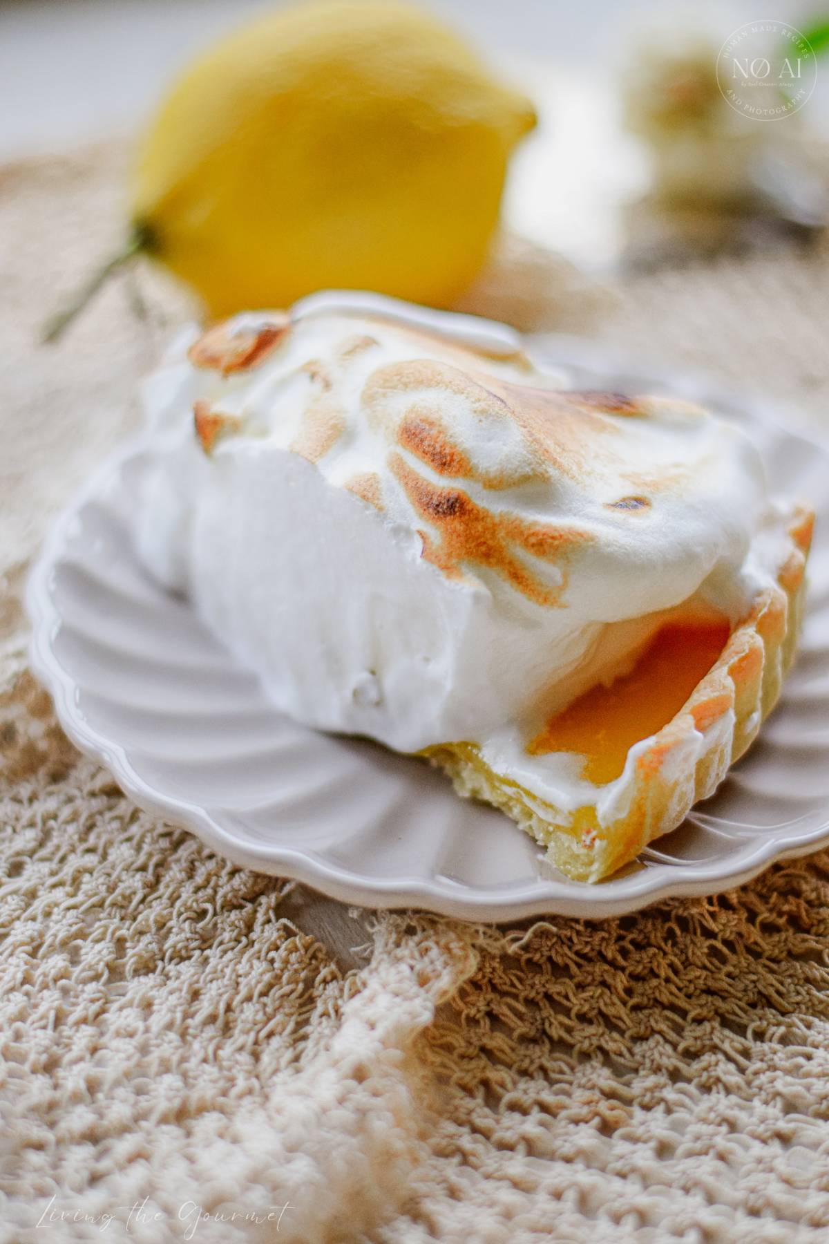 A homemade Lemon Meringue Tart with a buttery pastry crust filled with silky fresh lemon curd and topped with toasted Italian meringue, served on a white cake stand with fresh lemons and soft summer décor.