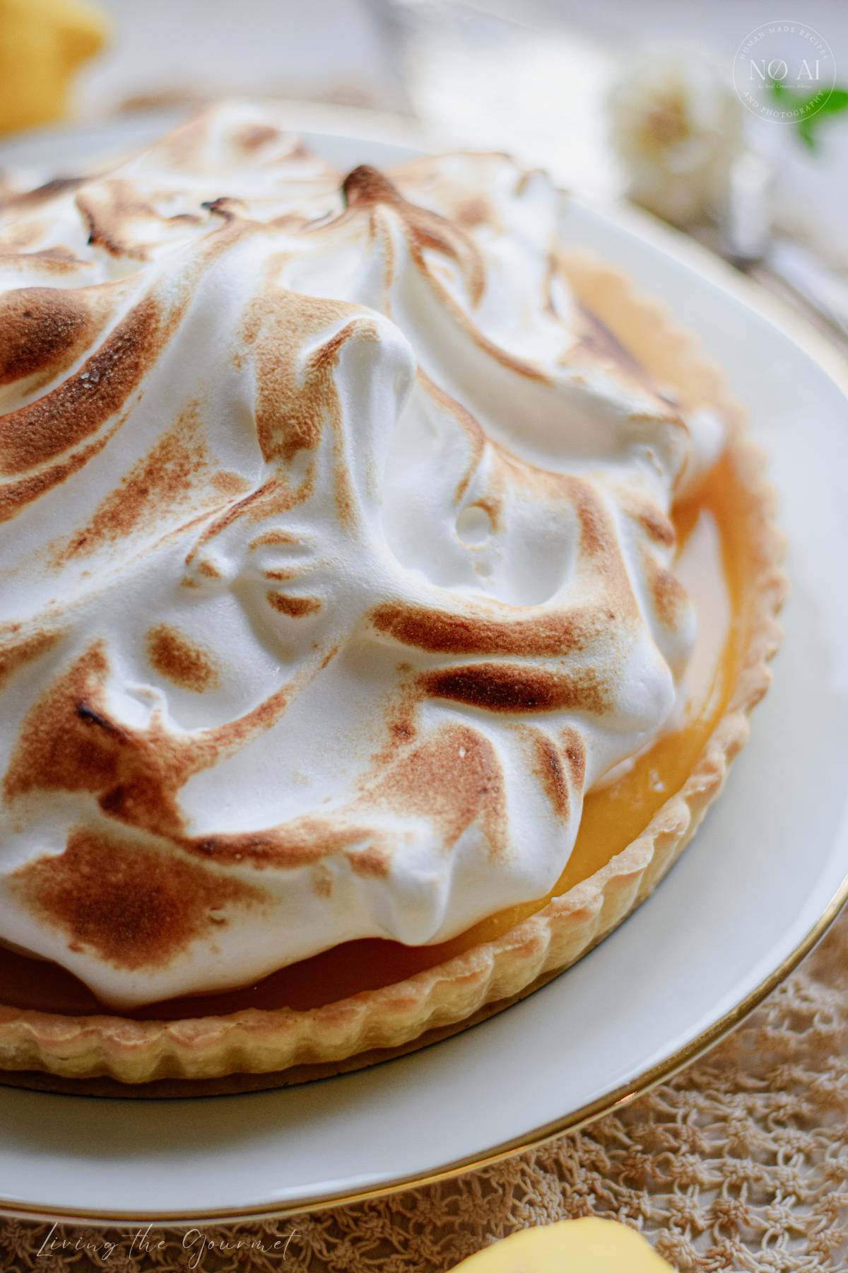 A homemade Lemon Meringue Tart with a buttery pastry crust filled with silky fresh lemon curd and topped with toasted Italian meringue, served on a white cake stand with fresh lemons and soft summer décor.