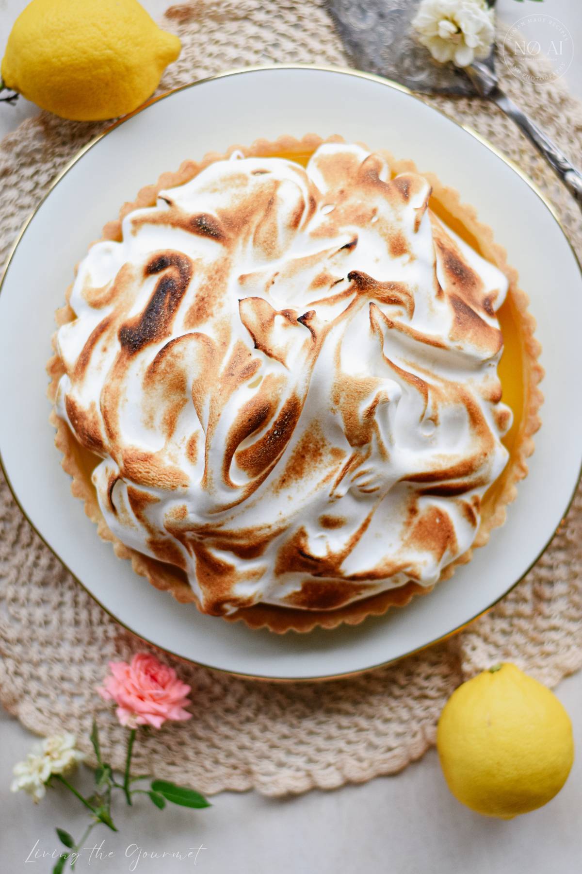 A homemade Lemon Meringue Tart with a buttery pastry crust filled with silky fresh lemon curd and topped with toasted Italian meringue, served on a white cake stand with fresh lemons and soft summer décor.