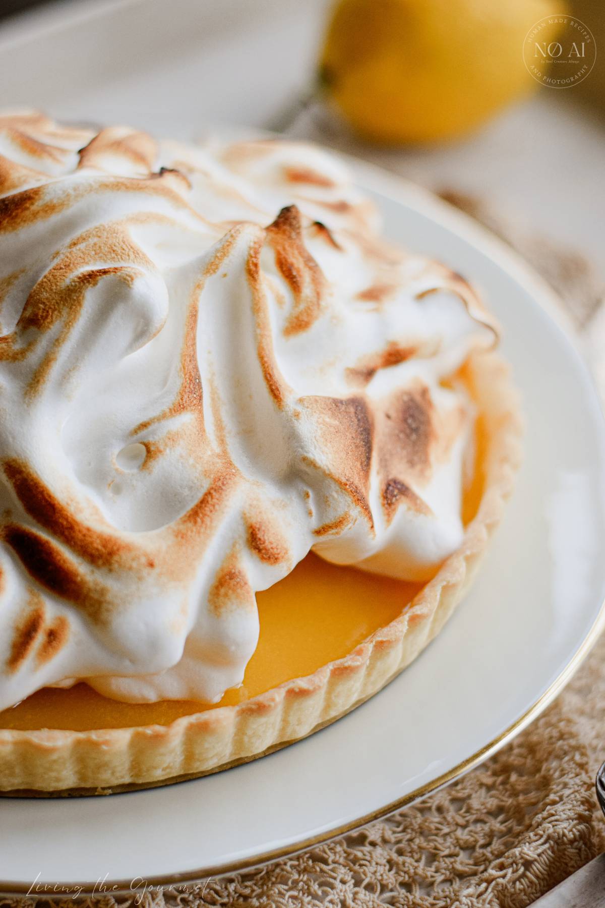 A homemade Lemon Meringue Tart with a buttery pastry crust filled with silky fresh lemon curd and topped with toasted Italian meringue, served on a white cake stand with fresh lemons and soft summer décor.